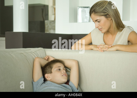 Ragazzo sdraiato sul divano a parlare con la madre che guarda a lui Foto Stock