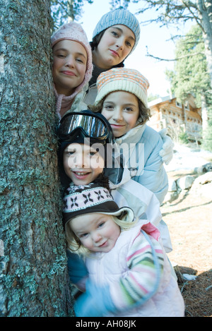 Gruppo di adolescenti e bambini vestiti in abiti invernali, ponendo accanto ad albero, ritratto Foto Stock