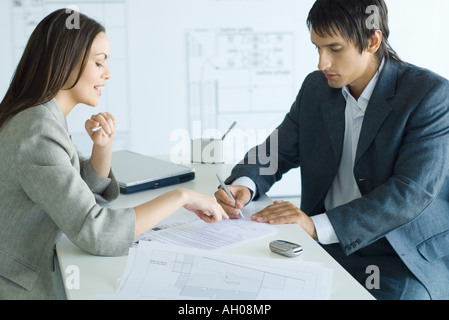 Femmina di agente immobiliare puntano al documento, uomo firma, blueprints in primo piano e sullo sfondo Foto Stock