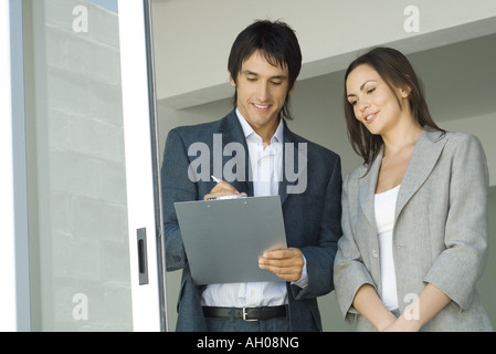 Maschio di agente immobiliare che mostra house a femmina client, iscritto negli appunti Foto Stock
