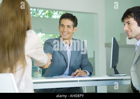 Coppia giovane seduto di fronte desk dal proprietario, donna stringono le mani con il proprietario Foto Stock