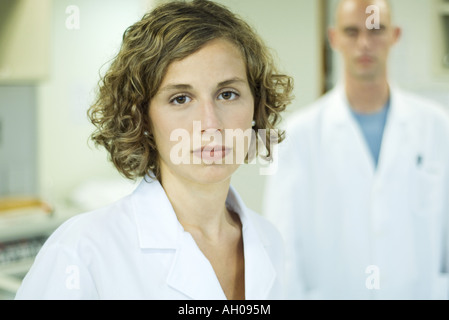 Medico donna guardando la telecamera, il collega di sesso maschile in background, ritratto Foto Stock