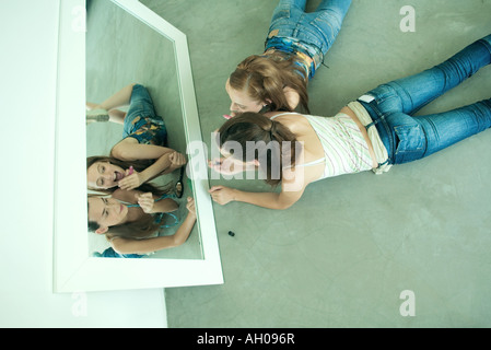 Due giovani amici che giace a terra e guardando se stessi in uno specchio, tenendo il rossetto, vista da sopra direttamente Foto Stock