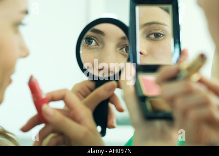 Due giovani amici guardando in sé gli specchi a mano, tenendo il rossetto, vista ritagliata Foto Stock