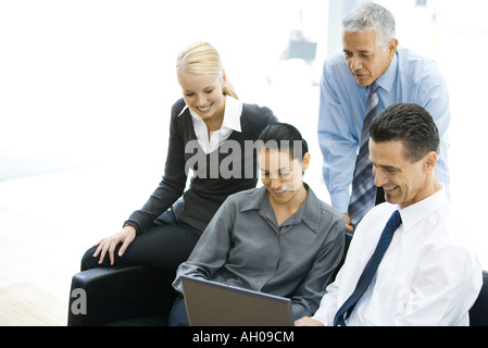 Quattro business associates guardando al computer portatile insieme sorridente Foto Stock