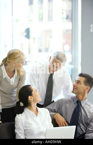 Quattro soci di affari sorridente ad ogni altro, uno utilizzando il computer portatile Foto Stock