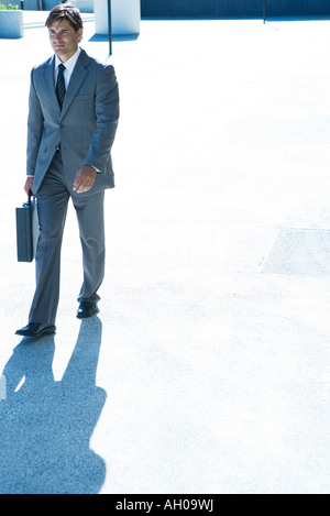 Giovane imprenditore passeggiate all'aperto, valigetta porta a piena lunghezza Foto Stock