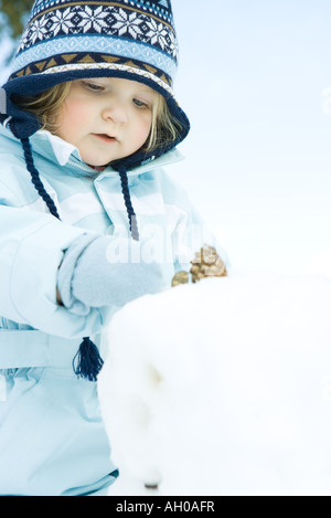 Il Toddler girl edificio pupazzo di neve, vestito in abiti invernali Foto Stock