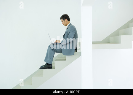 Uomo seduto sulle scale, utilizzando laptop Foto Stock