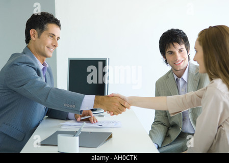 Imprenditore stringono le mani con la giovane donna di fronte desk, giovane donna compagno maschio sorridente Foto Stock