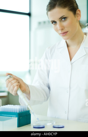 Giovane donna che lavorano nel laboratorio scientifico, tenendo un contagocce su piastra di Petri, guardando la fotocamera Foto Stock