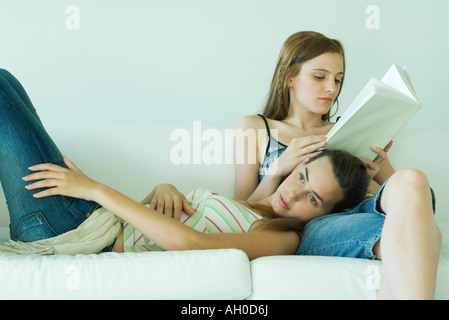 Giovane donna sulla lettura del lettino prenota, amico appoggiato la testa sul suo giro Foto Stock