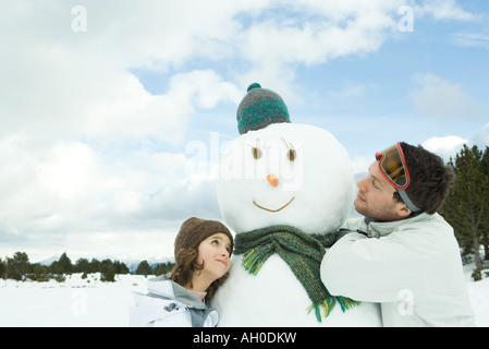 Fratello e Sorella abbracciando pupazzo di neve, sorridente, testa e spalle Foto Stock