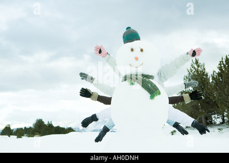 Giovani amici di nascondersi dietro pupazzo di neve, braccia tese Foto Stock