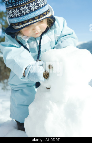Il Toddler girl edificio pupazzo di neve, vestito in abiti invernali Foto Stock