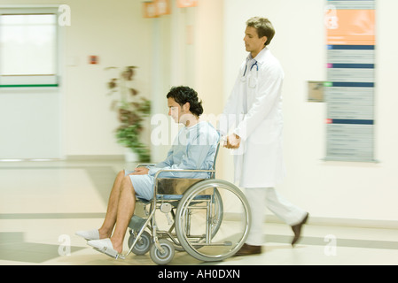 Medico maschio spingendo l uomo in carrozzella, a piena lunghezza Foto Stock