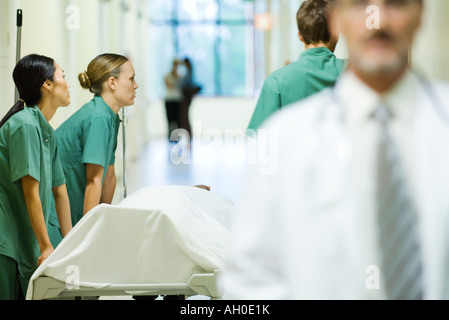 Il personale medico spingendo barella, guardando lontano, medico a piedi in primo piano Foto Stock