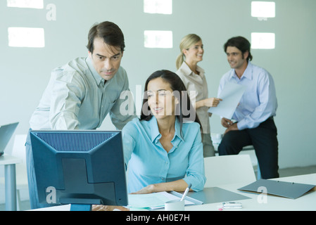 Imprenditore e imprenditrice in ufficio, guardando il computer associates in background Foto Stock