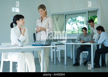 Due giovani imprenditrice in ufficio, chat, uomini d'affari in background Foto Stock