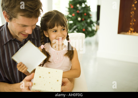 Ragazza seduta sull uomo di giro, apertura regalo di Natale, sorridente Foto Stock