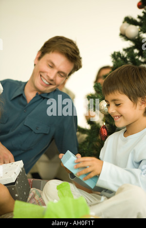 Uomo e ragazzo seduto da albero di Natale, apertura regalo di Natale, sorridente Foto Stock