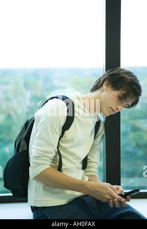 Studente maschio nella parte anteriore della finestra, guardando il telefono cellulare Foto Stock