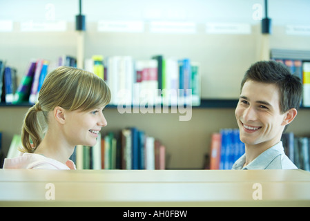 Due studenti nella biblioteca del campus accanto a scaffale, sorridente, testa e spalle Foto Stock