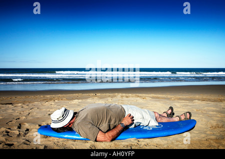 Uomo in hat posa su una tavola da surf in spiaggia Foto Stock