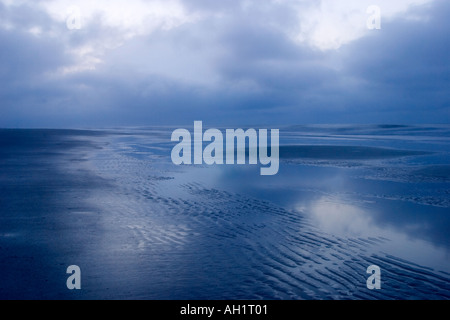 Spiaggia deserta con il grigio nuvole temporalesche riflesse Nello shallow pozze di marea sulla spiaggia Foto Stock