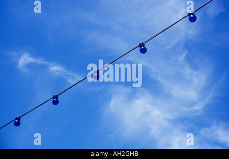 Una fila di lampadine blu infilate sotto un cielo blu con bianco wispy cirrus nuvole Foto Stock