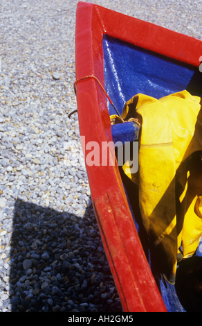 Dettaglio della prua di una di rosso e di blu dipinto di barca da pesca con giallo piegato telone e spiaggiata su ciottoli grigio Foto Stock