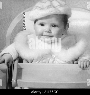 VINTAGE vecchia fotografia in bianco e nero SNAP SHOT della bambina indossa pelliccia cappotto rifilato e lana cofano seduto nella sedia alta Foto Stock