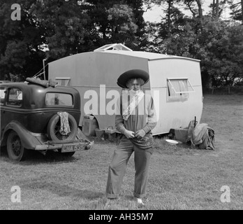 Vecchio VINTAGE IN BIANCO E NERO DI FAMIGLIA fotografia istantanea dell'uomo vestito in costume da cowboy IN PIEDI NELLA PARTE ANTERIORE DELLA VECCHIA AUTO E CARAVA Foto Stock