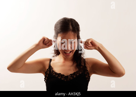 Giovane donna asiatica con le dita nei suoi orecchi per proteggerli da dolorose i livelli di rumore Aspetto del dolore da suoni eccessivi Foto Stock