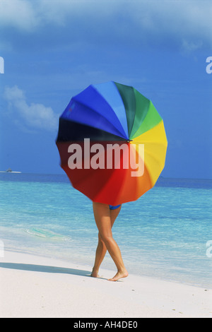 Donna che cammina sulla riva sabbiosa di filatura ombrellone colorato Foto Stock