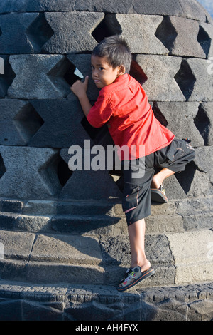 Giovane indonesiano ragazzo arriva a toccare le mani di Buddha per buona fortuna Borobudur Indonesia Foto Stock