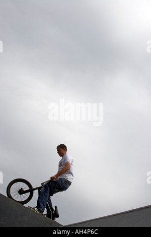 Giovane uomo o ragazzo facendo trick stunt salta su biciclette BMX da sotto contro il cielo grigio Foto Stock