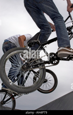 Giovani uomini o ragazzi facendo trick azione stunt salta in sella a biciclette BMX a metà in aria da sotto contro il cielo grigio Foto Stock