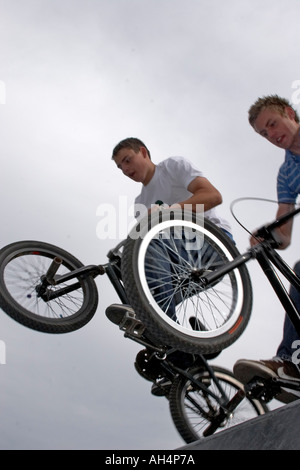 Giovani uomini o ragazzi facendo trick azione stunt salta in sella a biciclette BMX a metà in aria da sotto contro il cielo grigio Foto Stock