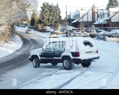 Essex automobilista con un minimo di visione posteriore guida su strade coperte di neve Road presso l'incrocio Foto Stock