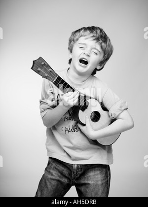 Ragazzo che finge di essere una rock star con piccoli bambini chitarra ukulele ukelel Foto Stock