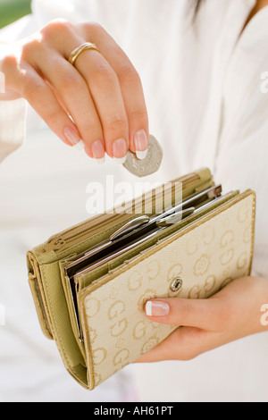 Giovane donna mettendo le monete in borsa Foto Stock