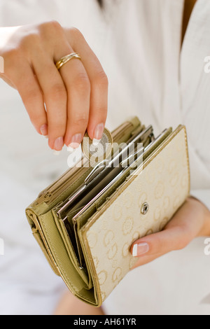 Giovane donna mettendo le monete in borsa Foto Stock