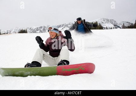 Metà donna adulta seduto sulla neve con una metà uomo adulto scorrere dietro di lei Foto Stock