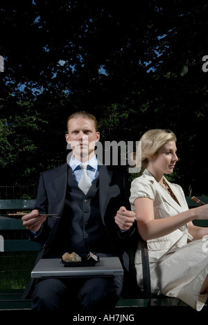 Giovane uomo seduto con una giovane donna su una panchina nel parco e mangiare sushi Foto Stock