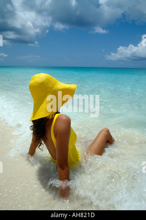 Turks e Caicos Provo donna nel cappello giallo e giallo suit siede in ocean surf Foto Stock