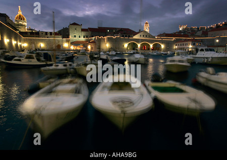 Barche di bob al tramonto su acqua in Dubrovnik porto illuminato dalle luci della città sulla costa mediterranea della Croazia Foto Stock