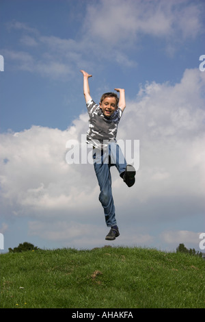 Dieci anni di old boy jumping braccia tese dietro. Foto Stock