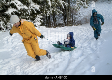 La madre ed i suoi due bambini giocando con una slitta nella neve in una località sciistica nelle Alpi francesi, Francia. Foto Stock