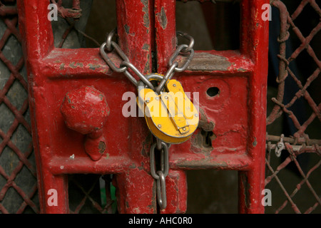 Un lucchetto giallo e una catena fissano i cancelli metallici rossi Foto Stock